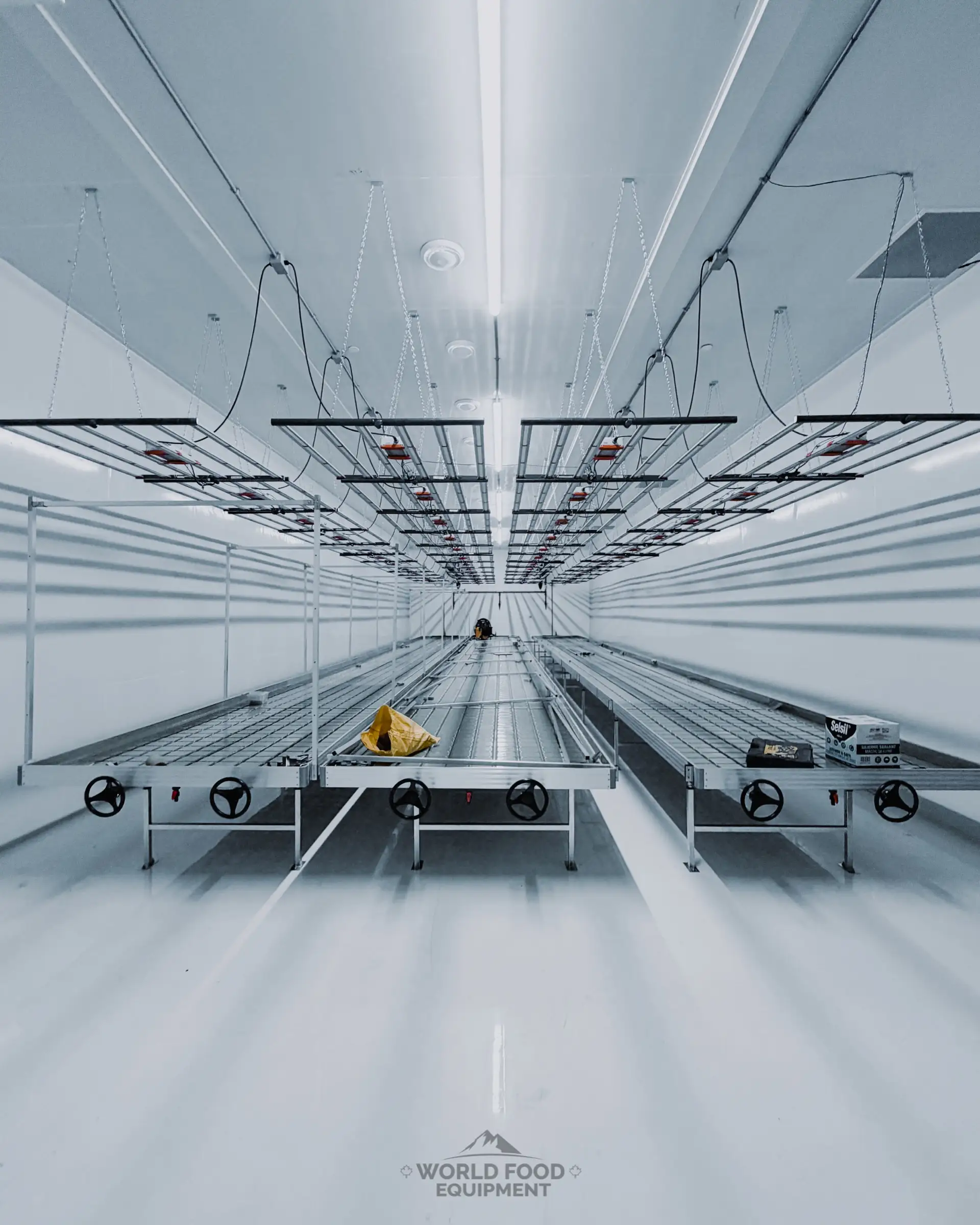 Finished cannabis cultivation cold room at 35 Silton with white rolling benches on tracks, LED grow-light rails overhead, white insulated-panel walls and ceiling, sealed floor, World Food Equipment Ontario cannabis cold storage built inside the secure perimeter