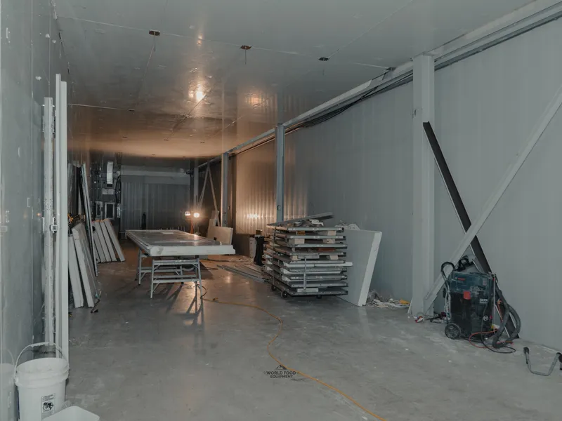 Sawhorse cutting station inside the 35 Silton cold storage envelope with an insulated panel laid out for measuring and cutting, stacked panels and a Bosch shop-vac on the floor, insulated walls in the background.