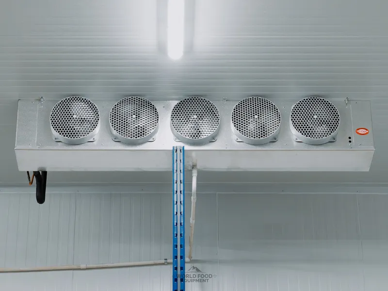 Trenton five-fan ceiling-mounted evaporator at Atlas Foods, clean close-up of the unit with the cooler ceiling panel above and a refrigeration line dropping down to the Heatcraft condenser, one of four sized to specialty-food-distribution throughput, Toronto.