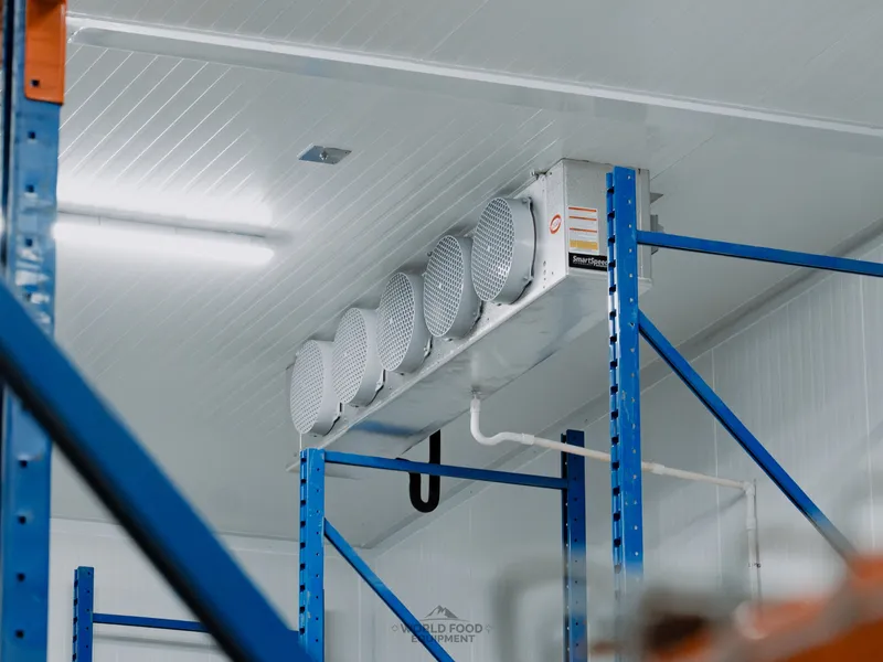 SmartRefer ceiling-mounted evaporator overhead at Atlas Foods with tall blue and orange pallet racking framing the rack aisle, cold air dropping directly over the rack lanes inside the 3,000 sq ft cooler.