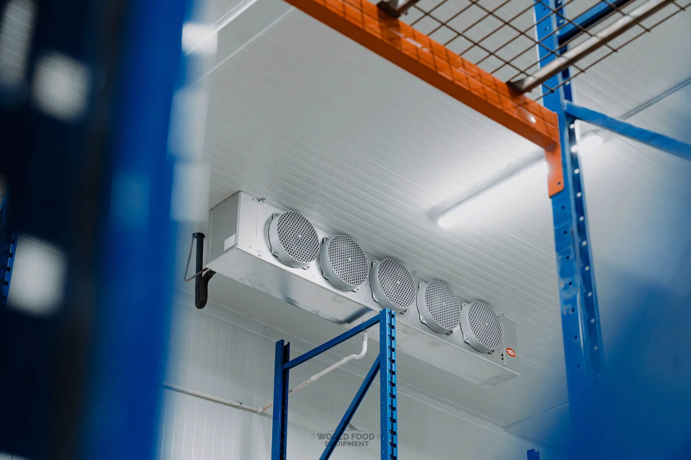 Industrial-scale commercial cold storage with ceiling-mounted five-fan evaporator between blue and orange pallet racking, Atlas install, Ontario, World Food Equipment