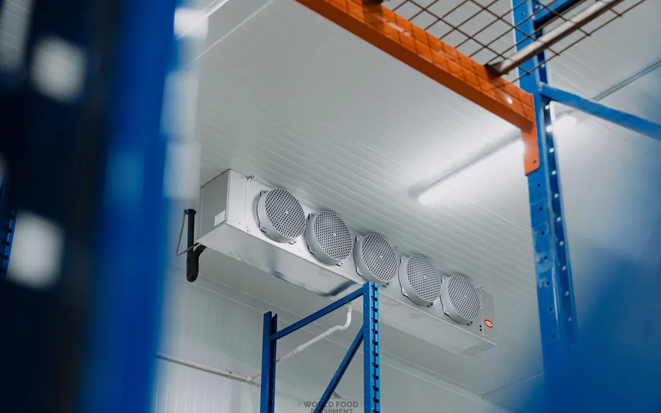 Ceiling-mounted five-fan evaporator unit between blue and orange industrial pallet racking in a finished commercial cold storage facility, Atlas install, Ontario, World Food Equipment.