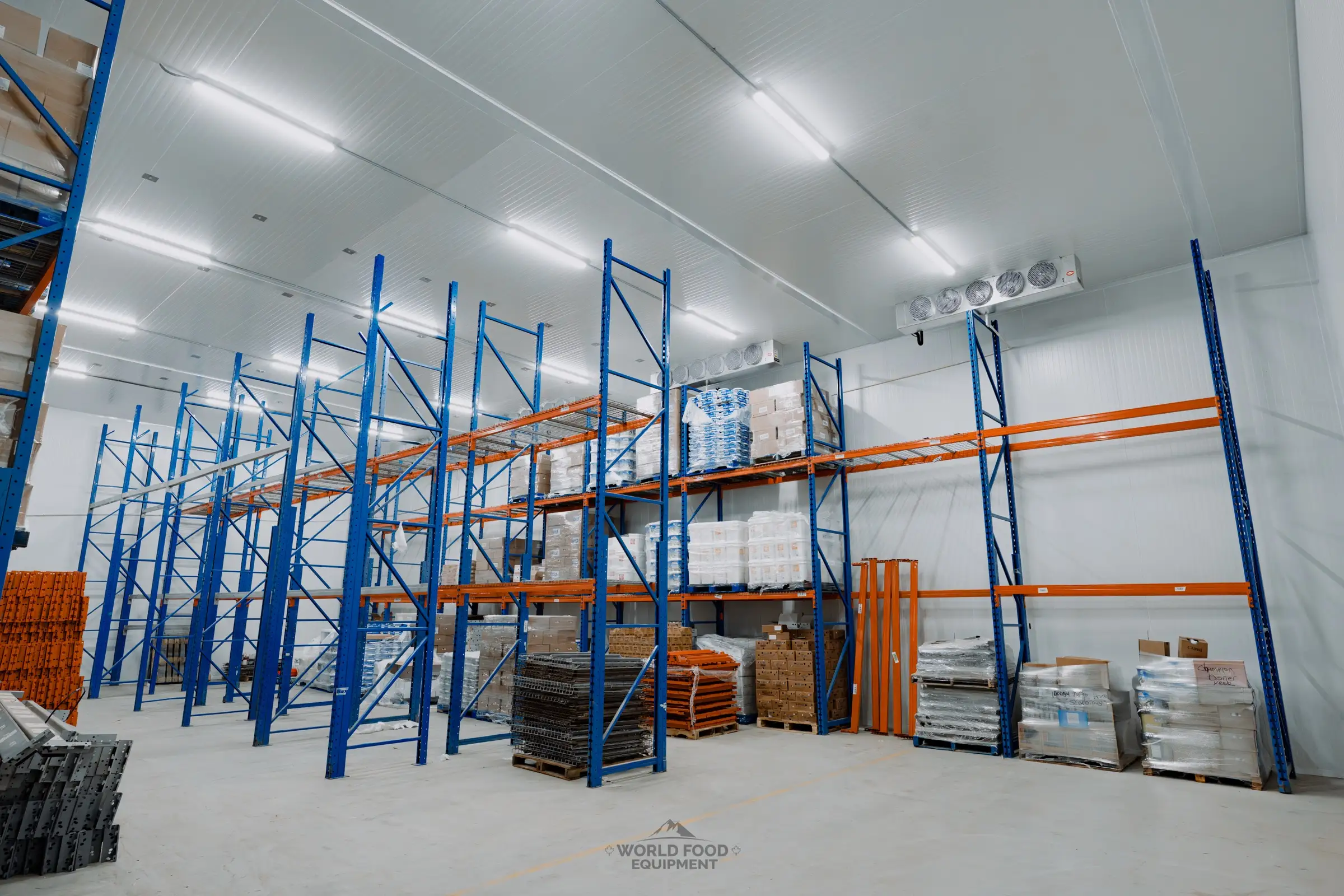 Atlas Foods 3,000 sq ft walk-in cooler operational at day-30 handoff, blue and orange pallet racking floor to ceiling with early product on the lower tiers, ceiling-mounted evaporators visible above.