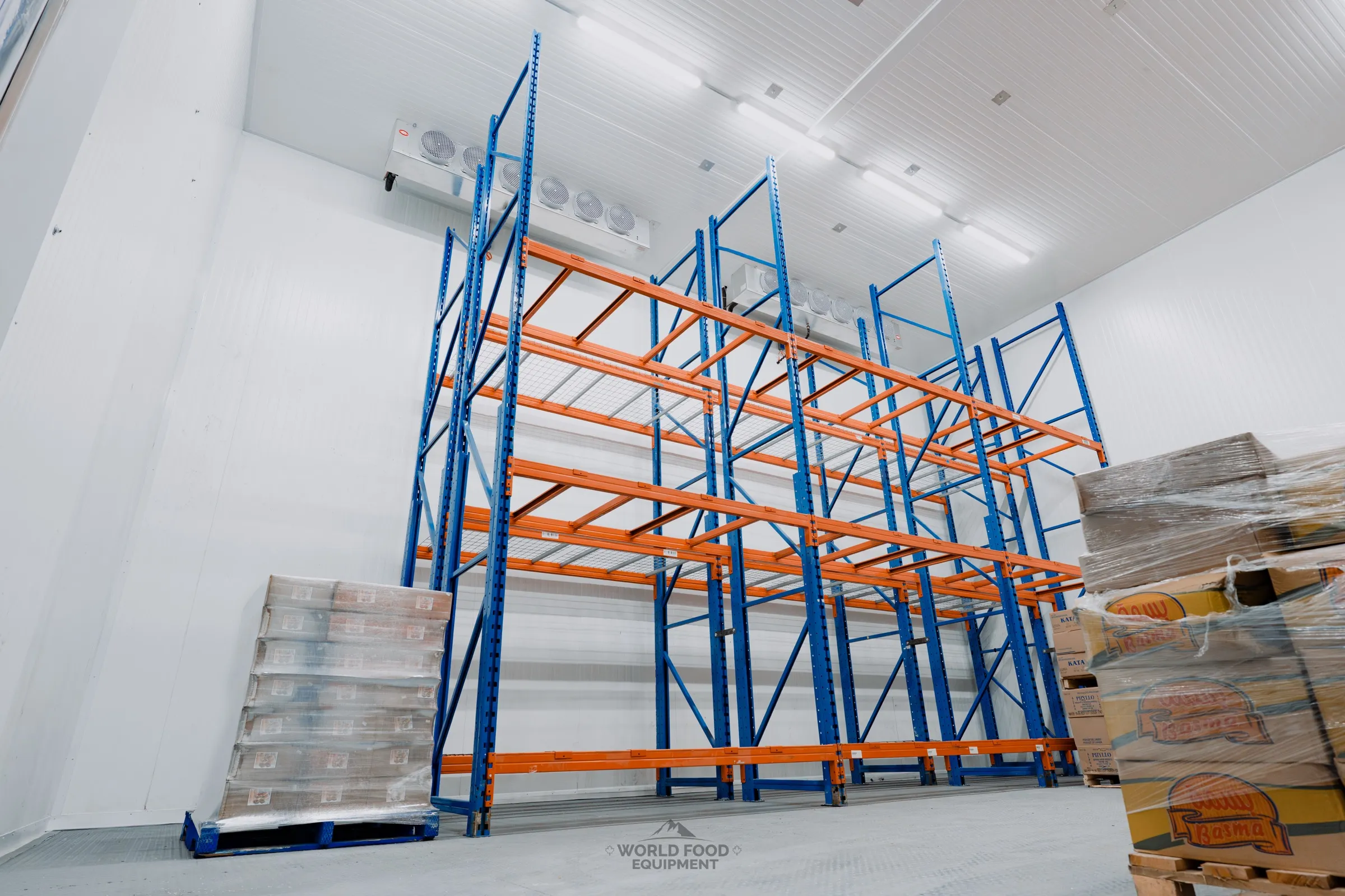 Finished commercial cold storage room with industrial orange pallet racking on both sides, ceiling-mounted evaporators visible on the back wall, a stack of orange beam stock on the right, Atlas install, Ontario commercial walk-in installation by World Food Equipment