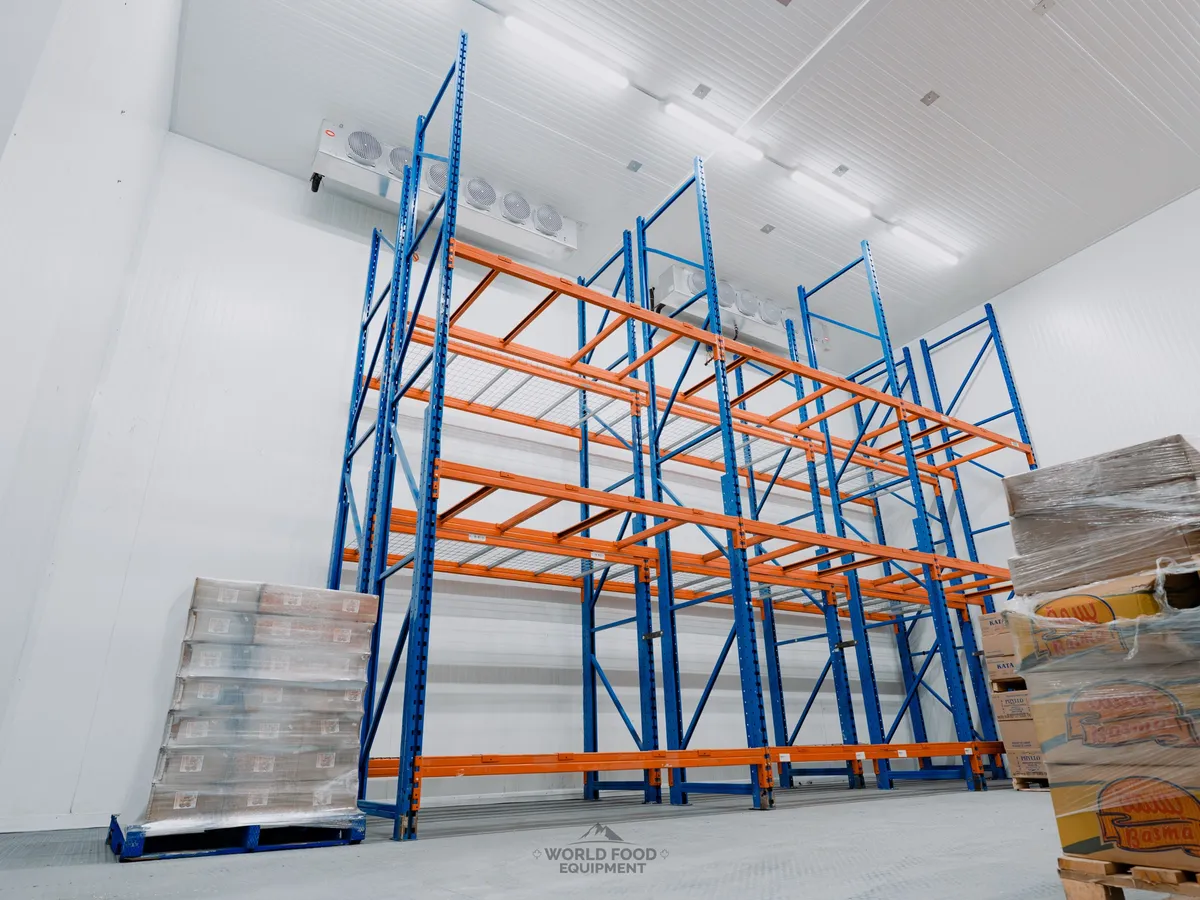 Atlas Foods walk-in cooler at WFE handoff: tall blue and orange pallet racking installed end to end, multiple ceiling-mounted evaporators visible at the top of the room, refrigeration running and the room pulled down to spec, ready for Atlas to stock specialty food distribution product.
