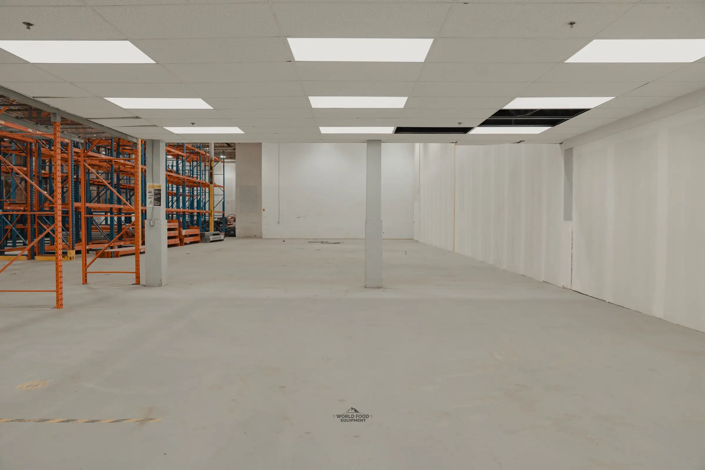 Atlas Foods Toronto warehouse on day one with drop ceiling, open floor, and orange pallet racking pre-positioned outside the future cold storage envelope.