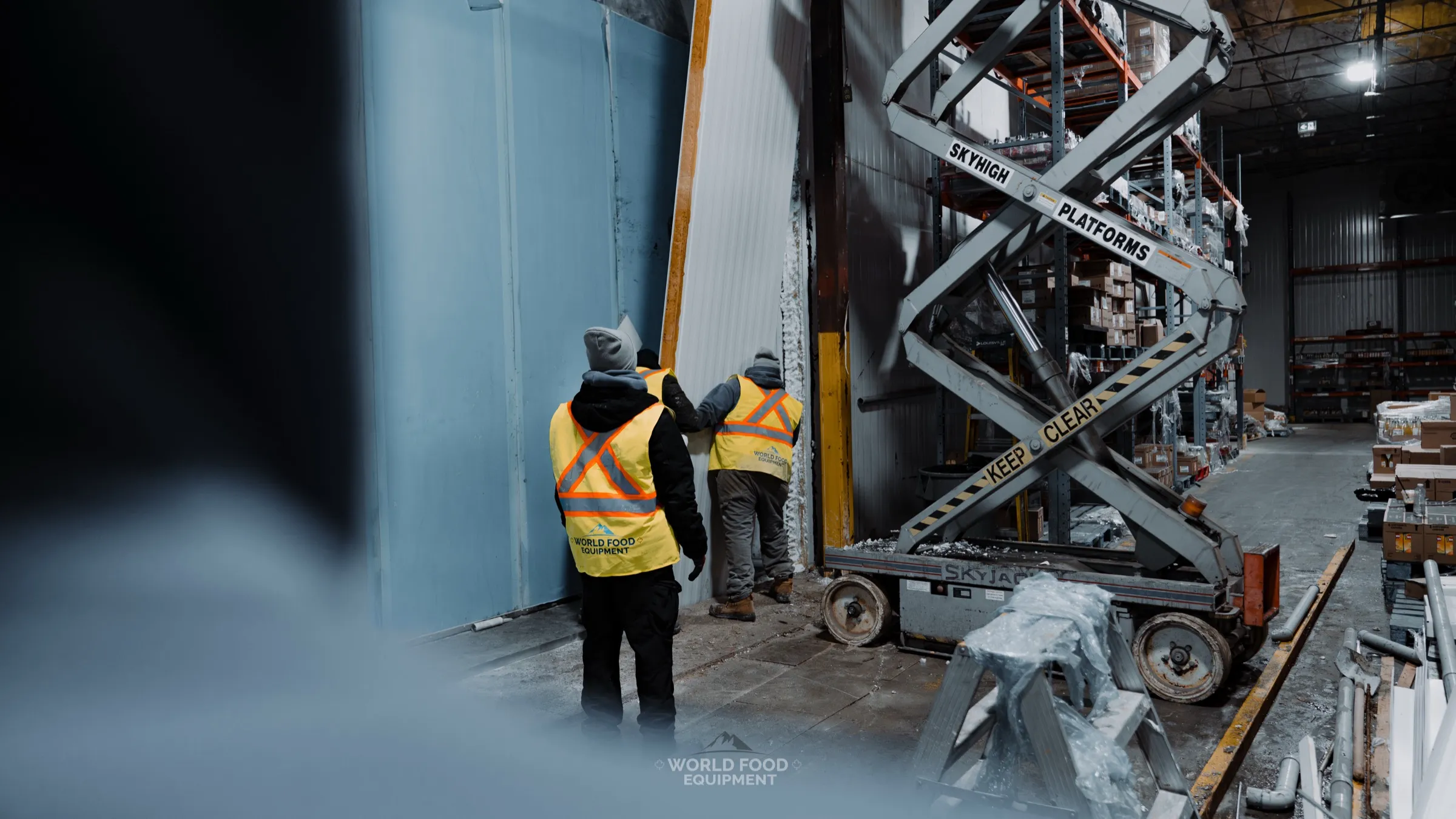 WFE crew setting a new insulated panel with a scissor lift during the 140 ft freezer wall rebuild at CJR Grocers, executed while the grocery facility stayed open.