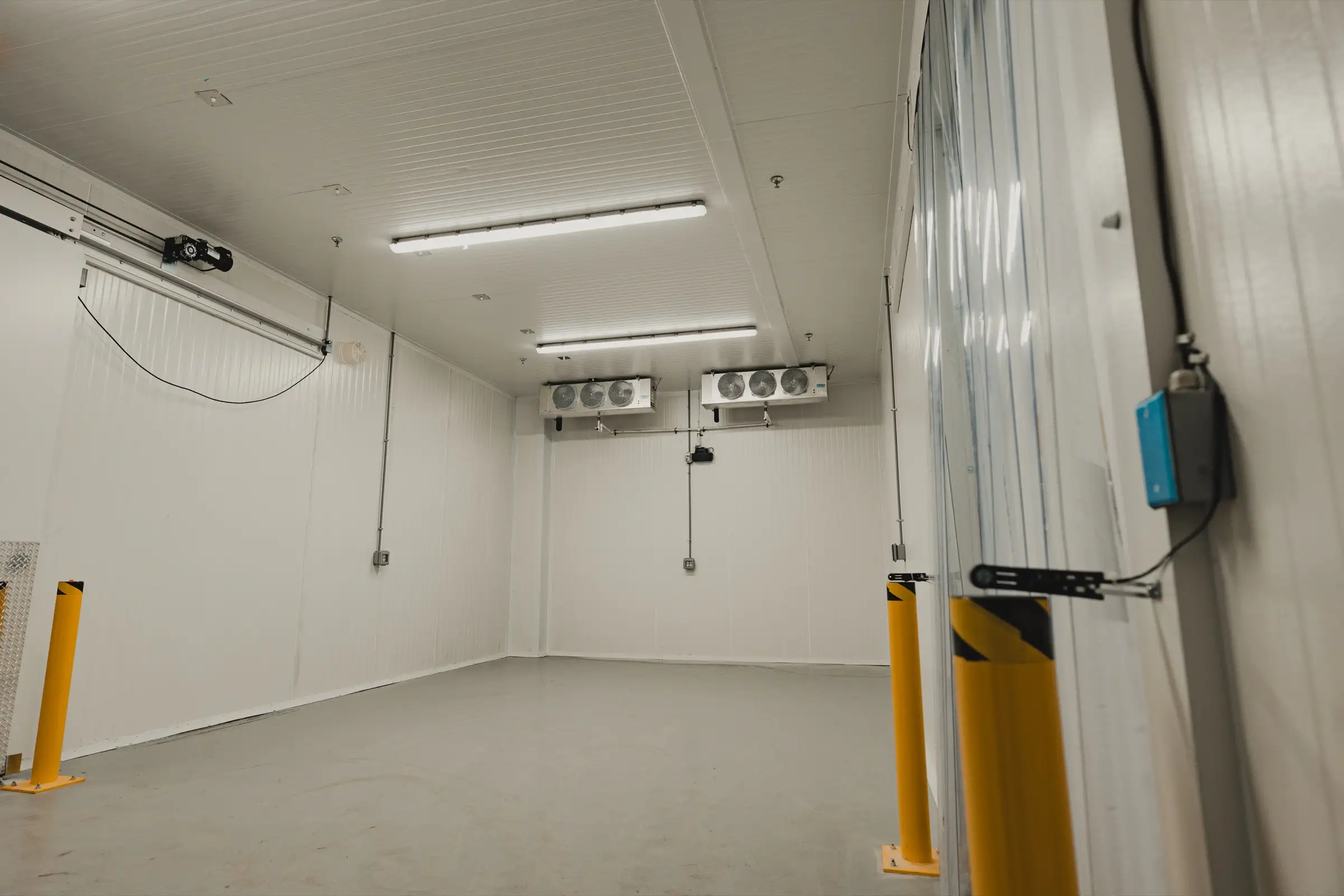 SKOR Crestlawn operational walk-in freezer: dual ceiling-mounted evaporators, yellow safety bollards at the doorway, refrigeration commissioned.