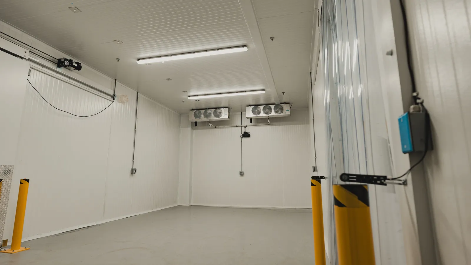 Finished walk-in cooler interior with evaporators mounted on the ceiling and a plastic strip curtain at the doorway, SKOR Crestlawn install, Ontario, World Food Equipment