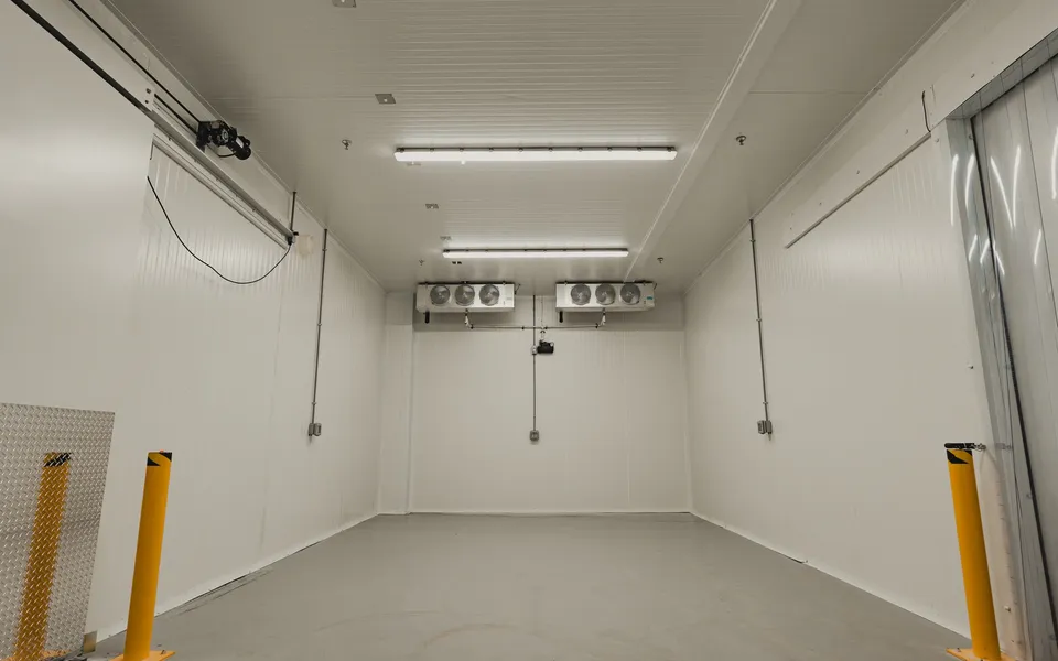 Finished walk-in cold storage interior with dual ceiling-mounted KeepRite evaporators, vinyl strip curtain at the entry, and white insulated panel walls, SKOR Crestlawn install, Ontario, World Food Equipment