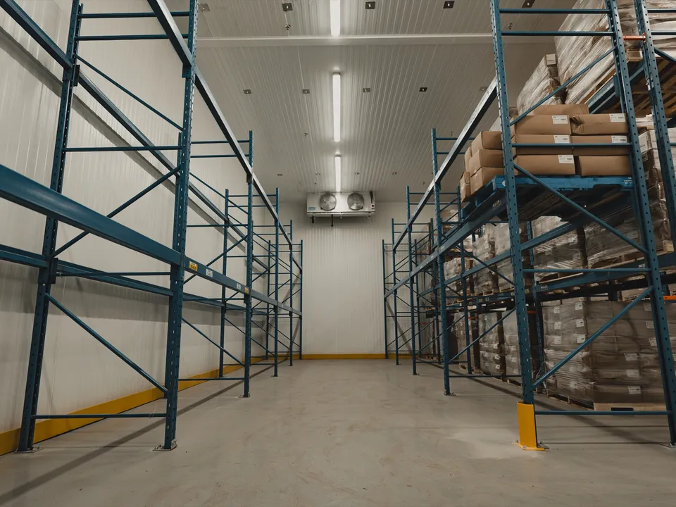 Operational interior of the SKOR Crestlawn walk-in freezer with stocked blue pallet racking, dual ceiling-mounted evaporators, school food supplier in production.