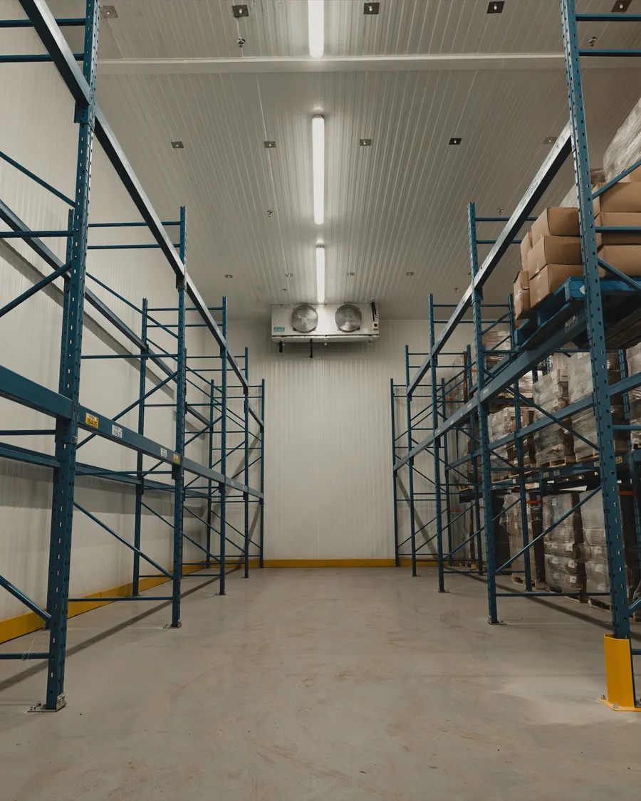Operational walk-in cooler interior with blue industrial pallet racking on both sides loaded with product, SKOR Crestlawn install, Ontario, World Food Equipment