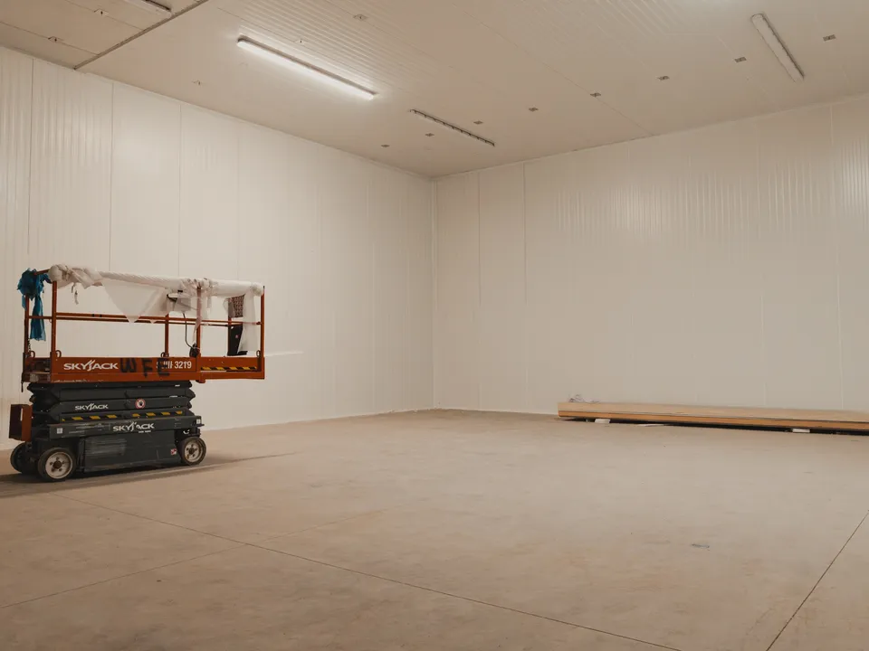 Walk-in freezer envelope at SKOR Crestlawn with white insulated panel walls and ceiling already in place, SkyJack scissor lift staged inside the empty room for the next phase of work, school food supplier facility.