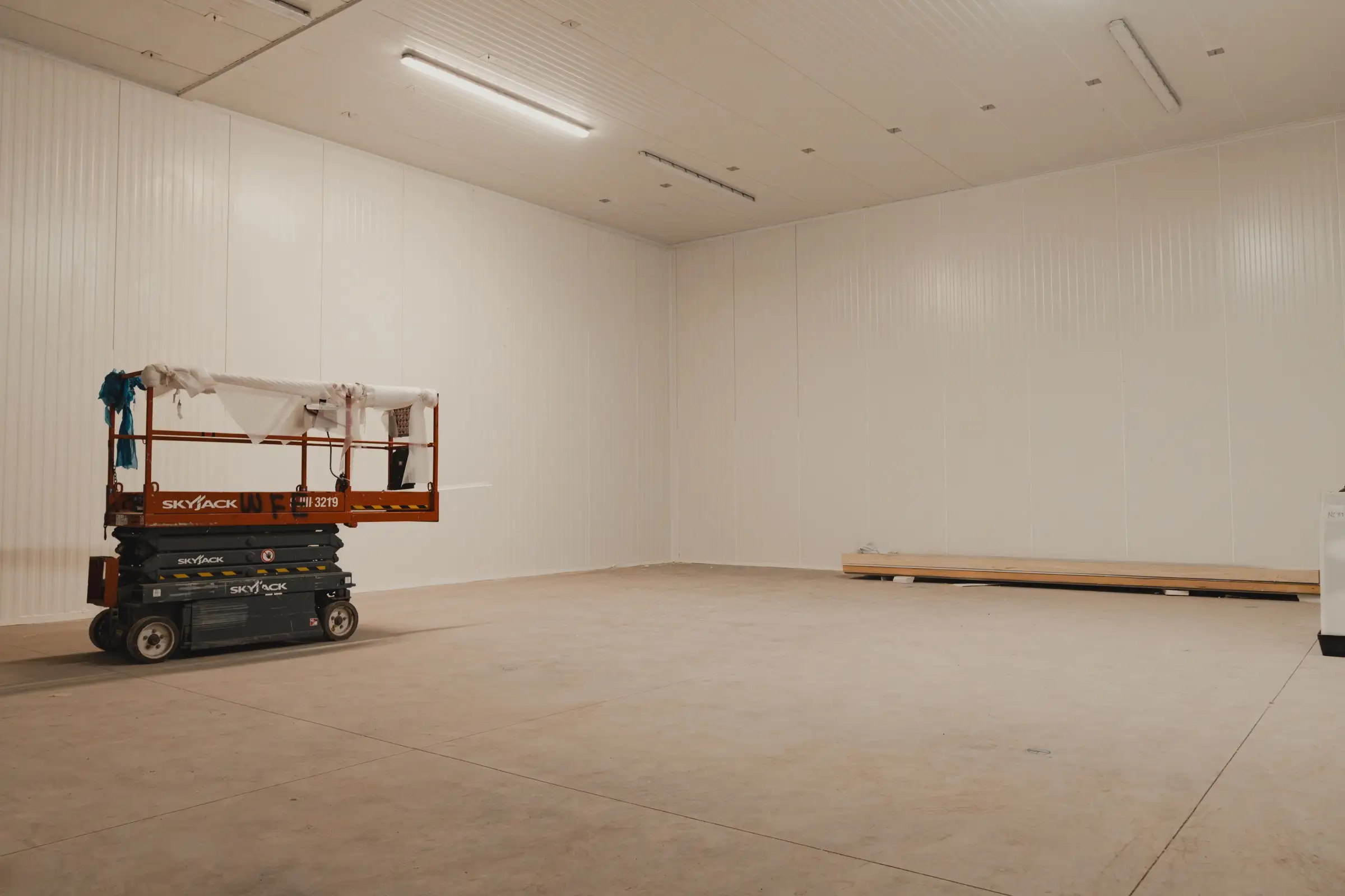 Walk-in freezer envelope at SKOR Crestlawn during the Nov 7 build week with white insulated panel walls and ceiling already in place, SkyJack scissor lift staged inside the empty room before refrigeration and doors were installed.