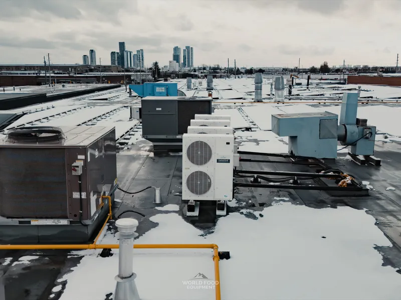 Rooftop view of the Food Junction Toronto building with multiple refrigeration condensing units, HVAC equipment, and ductwork installed across the snow-covered roof, downtown Toronto skyline rising in the distance.