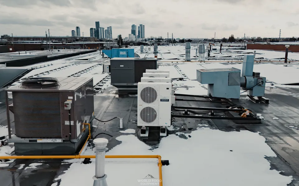 Rooftop of a Mississauga food hall after a World Food Equipment install: a Copeland Scroll outdoor refrigeration condensing unit on rubber isolators, a packaged rooftop HVAC unit, an exhaust fan, and a yellow-painted gas line across a snow-dusted flat roof