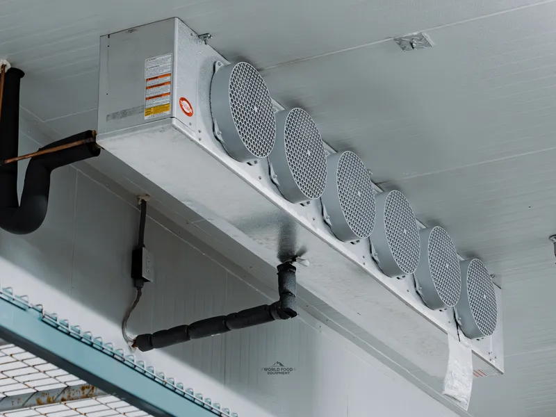 KRACK seven-fan ceiling-mounted evaporator close-up at Food Junction Toronto, larger industrial refrigeration unit with seven round meshed fans in a row, drain line wrapped beside it, white ceiling panel above.