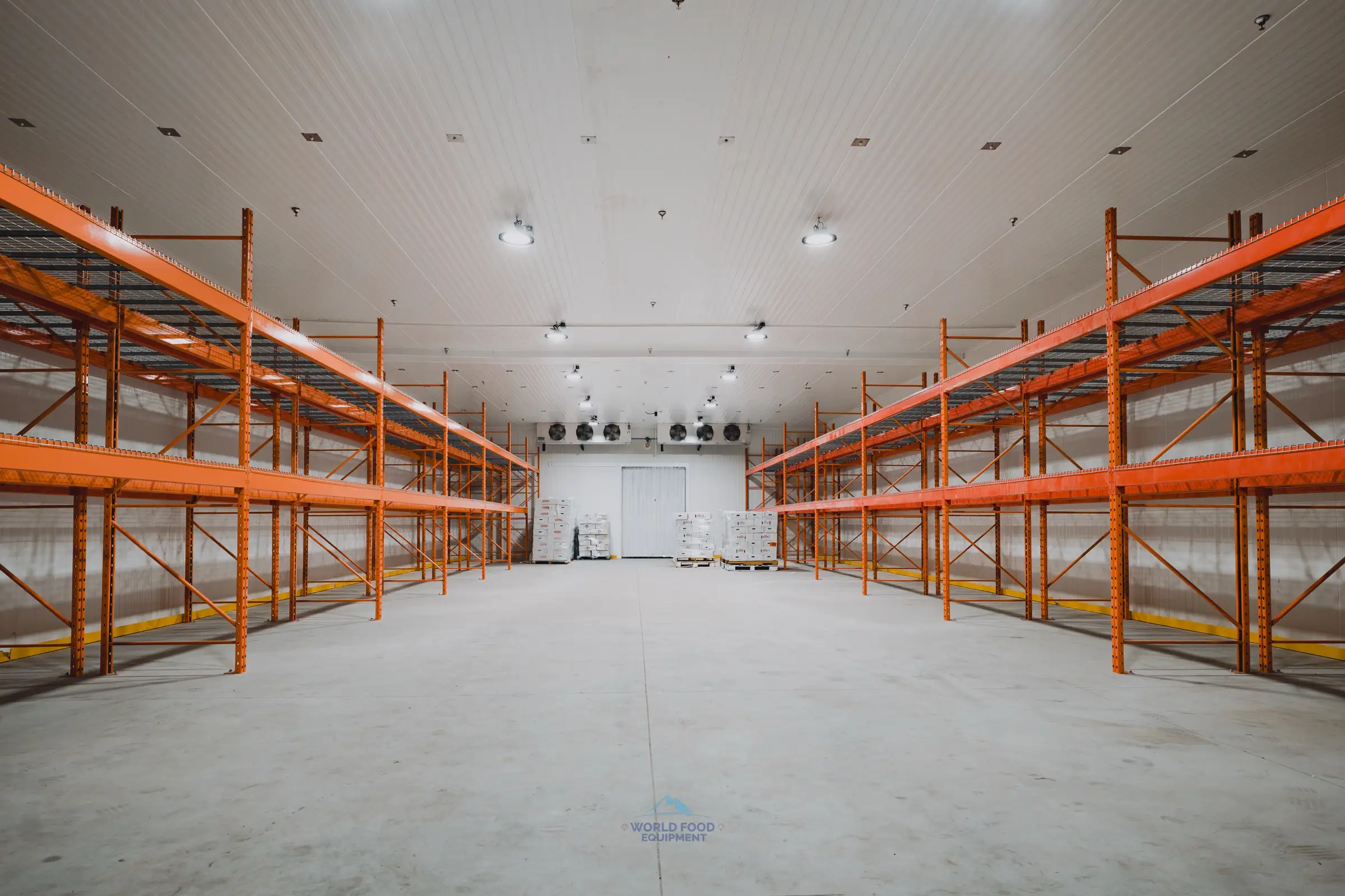 Finished walk-in freezer envelope at the halal meat processor in Mississauga, dual KeepRite ceiling-mounted evaporators commissioned at the far end, orange pallet racking installed and waiting for product, white insulated panels clean across the 10,000 sq ft envelope.