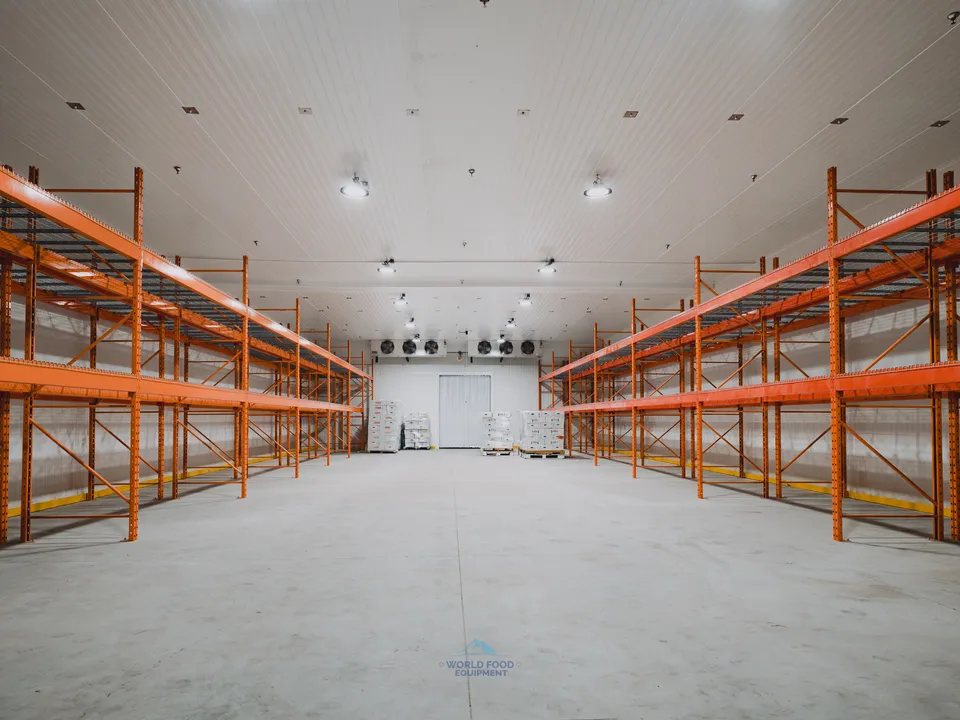 Finished walk-in freezer envelope at the halal meat processor in Mississauga, dual KeepRite ceiling-mounted evaporators commissioned at the far end, orange pallet racking installed and waiting for product, white insulated panels clean across the 10,000 sq ft envelope.