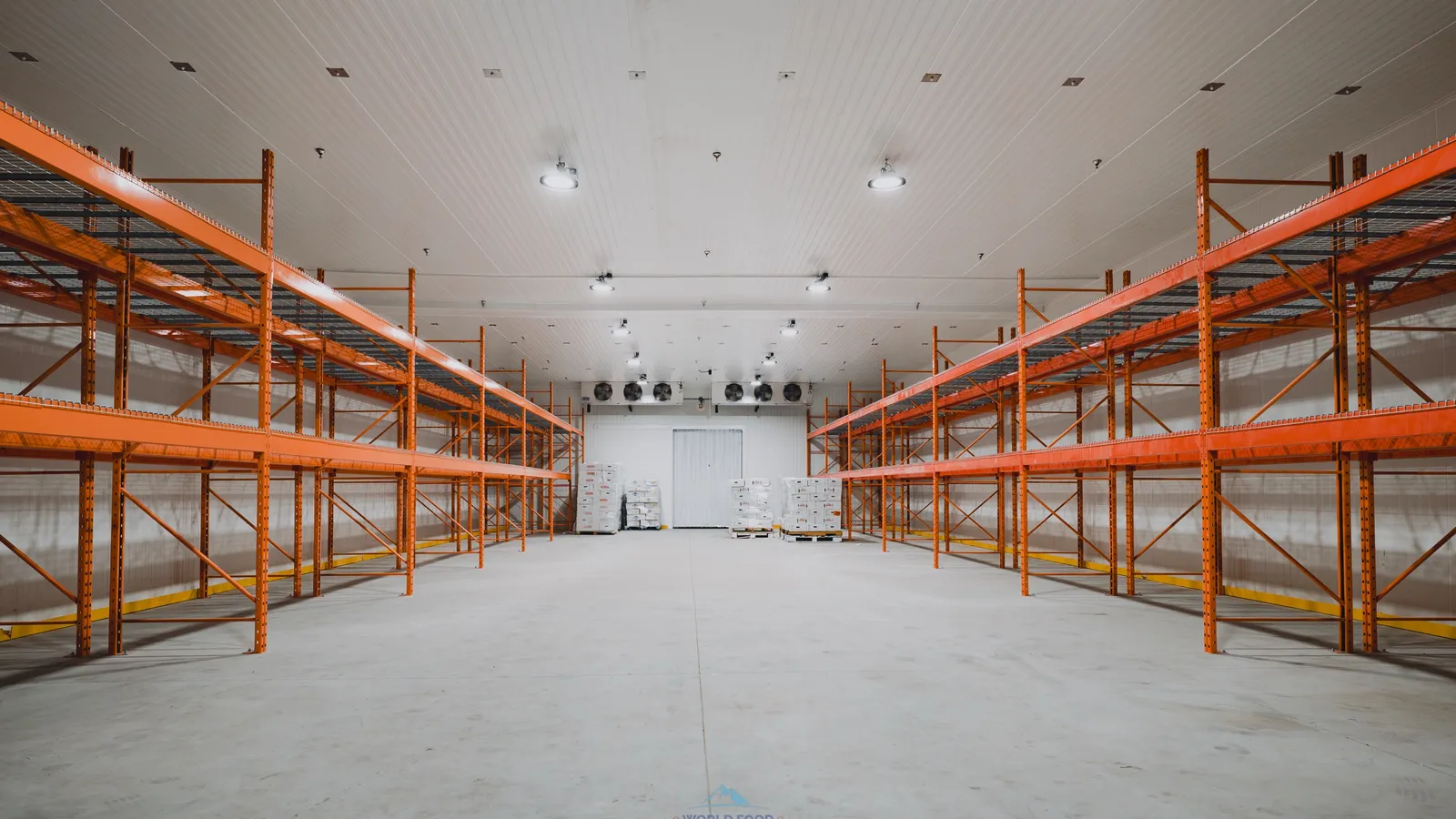 Operational commercial walk-in freezer with industrial orange pallet racking, ceiling-mounted evaporators visible at the back wall, Ontario meat-processing facility, World Food Equipment