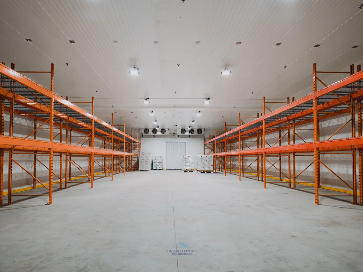 Finished walk-in freezer envelope at the halal meat processor in Mississauga as the WFE deliverable: dual KeepRite ceiling-mounted evaporators commissioned at the back wall, orange pallet racking installed and waiting for product, white insulated panel walls clean across the 10,000 sq ft envelope, polished concrete floor.