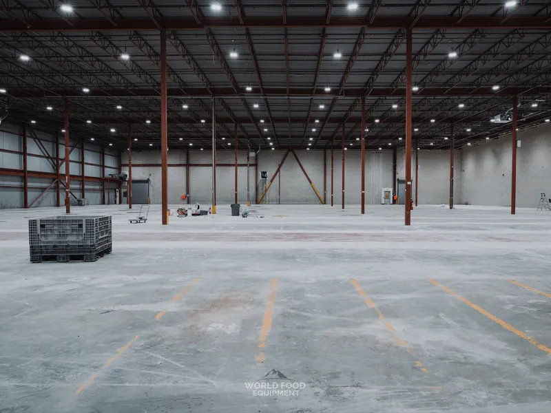 Wide interior of the cleared Longo's Scarborough distribution floor with a single grey bin in the foreground, structural columns running across the space, polished concrete floor cleared of all refrigeration.