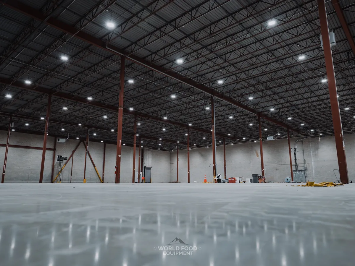 Cleared Longo's distribution floor in Scarborough after WFE's refrigeration decommissioning: low-angle architectural view of the structural column grid running across the empty space, polished concrete floor reflecting the columns, ceiling structure open above, full refrigeration plant removed.