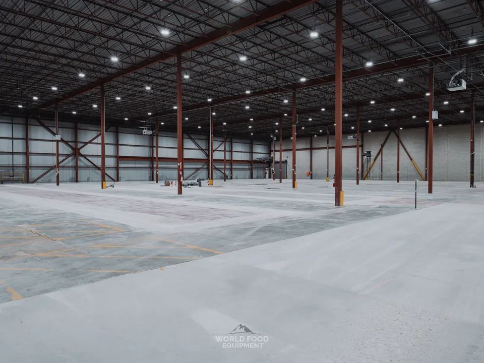 Cathedral-scale empty grocery distribution warehouse at the Longo's Scarborough site after WFE's full refrigeration decommissioning, red I-beam columns running the length of the building, single worker in the distance, polished concrete floor cleared of all refrigeration infrastructure.