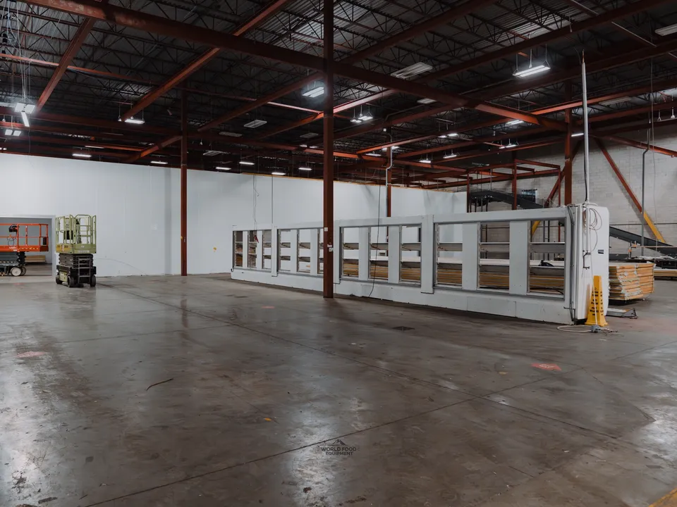 Long walk-in cooler box still in place inside the Longo's Scarborough warehouse with contents and refrigeration removed, scissor lift staged to the left, red I-beam ceiling structure visible above.