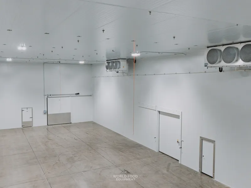 Smaller pharma-grade compartment inside the Pacer Air Freight medical-grade cold storage envelope in Mississauga with insulated swing door open at the left, dual KeepRite ceiling-mounted evaporators along the right wall, white insulated panel walls and ceiling clean, polished concrete floor.