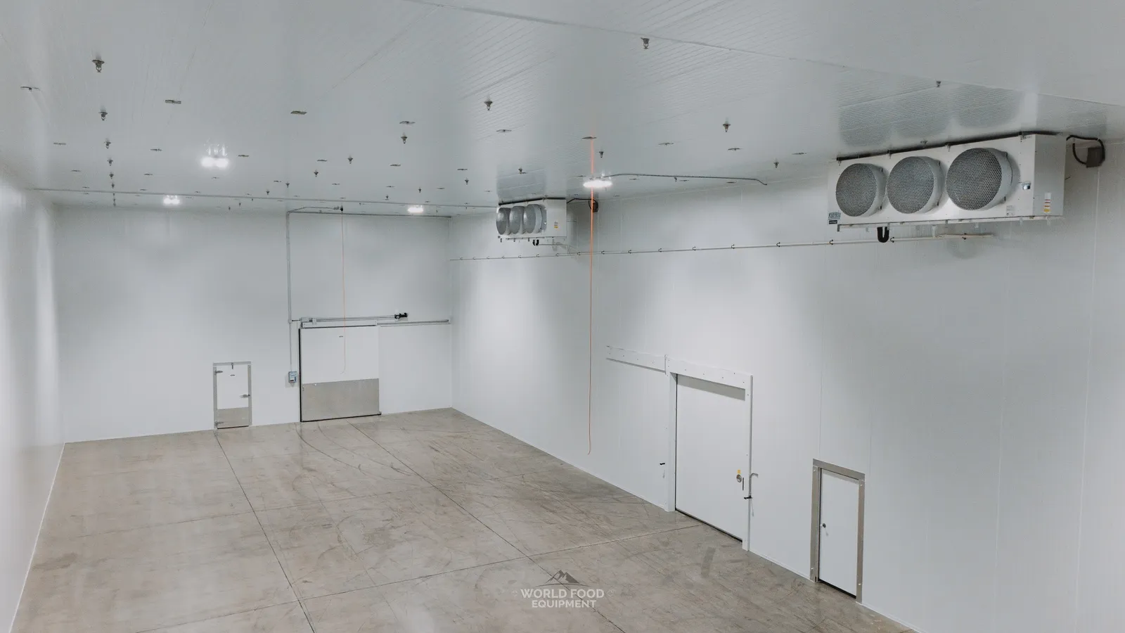Finished cathedral-scale industrial cold storage room with white insulated panel walls and ceiling, polished concrete floor, dual ceiling-mounted three-fan evaporators on the right wall, twin insulated walk-in doors at the back wall, Pacer Air Freight install, Ontario, World Food Equipment