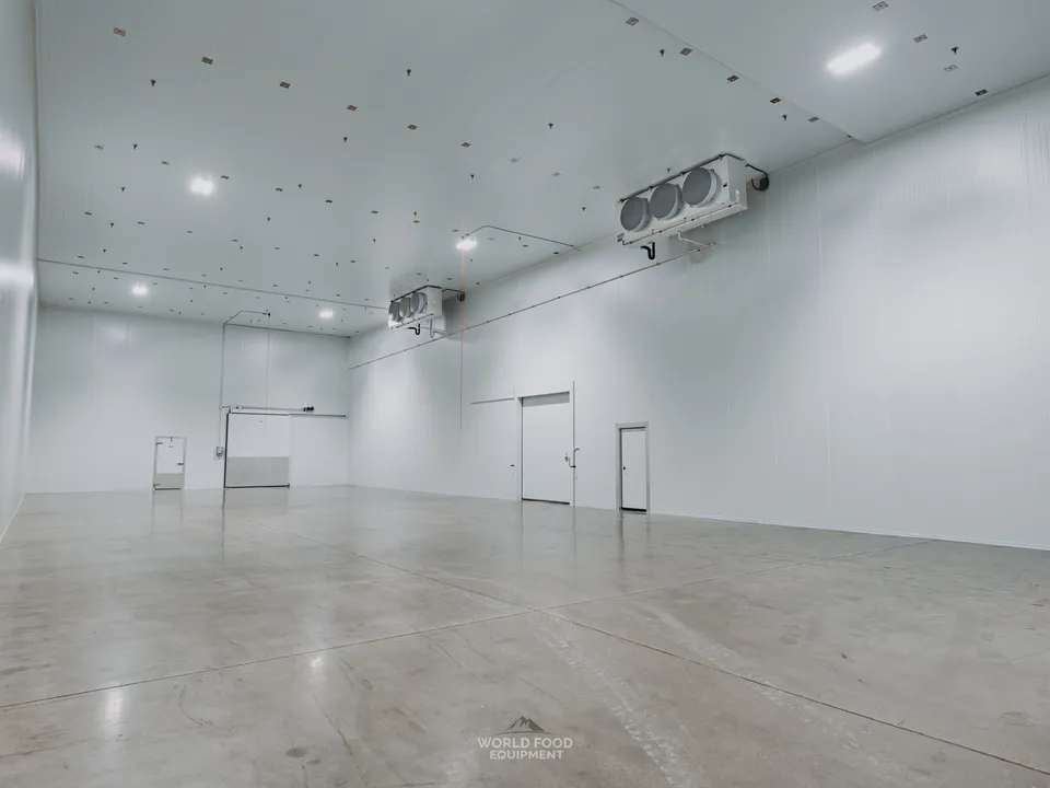 Cathedral-scale finished envelope at the Pacer Air Freight medical-grade cold storage in Mississauga: multi-zone KeepRite ceiling evaporators mounted along the right wall, polished concrete floor reflecting the structure, doorway visible mid-room, white insulated panel walls clean across the 10,000 sq ft envelope.