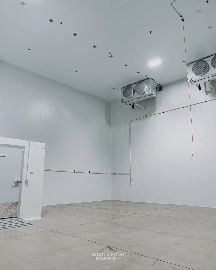 Heavy-duty insulated industrial cold storage door open with full-height bracing and ceiling evaporators visible on the right wall, Pacer Air Freight install, Ontario, World Food Equipment
