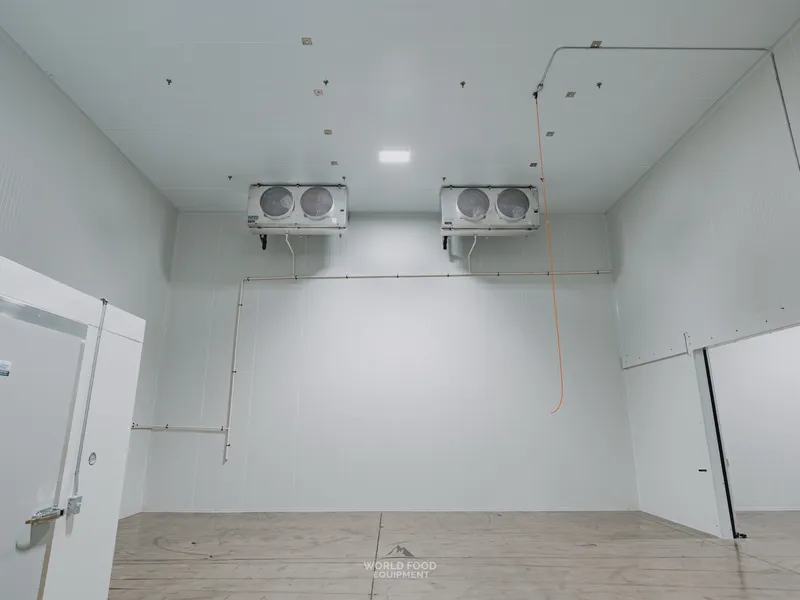 Smaller pharma-grade compartment inside the Pacer Air Freight medical-grade cold storage envelope in Mississauga with two ceiling-mounted KeepRite evaporators on the far wall, refrigeration lines routed in orange protective sleeving along the wall down to the floor.