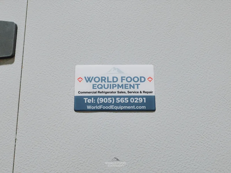 WFE service-line sticker close-up on a white insulated panel wall at the Pacer Air Freight cold storage envelope in Mississauga: World Food Equipment branded sticker with phone number and website.