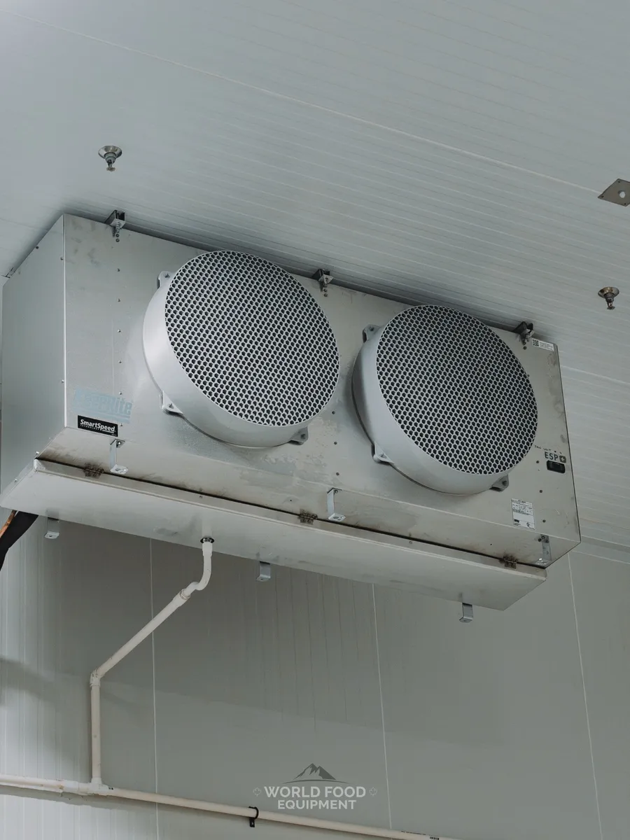 KeepRite SmartSpeed dual-fan evaporator mounted on a white insulated ceiling panel with copper line set and drain, Pacer Air Freight cold storage install, Mississauga, Ontario, World Food Equipment.