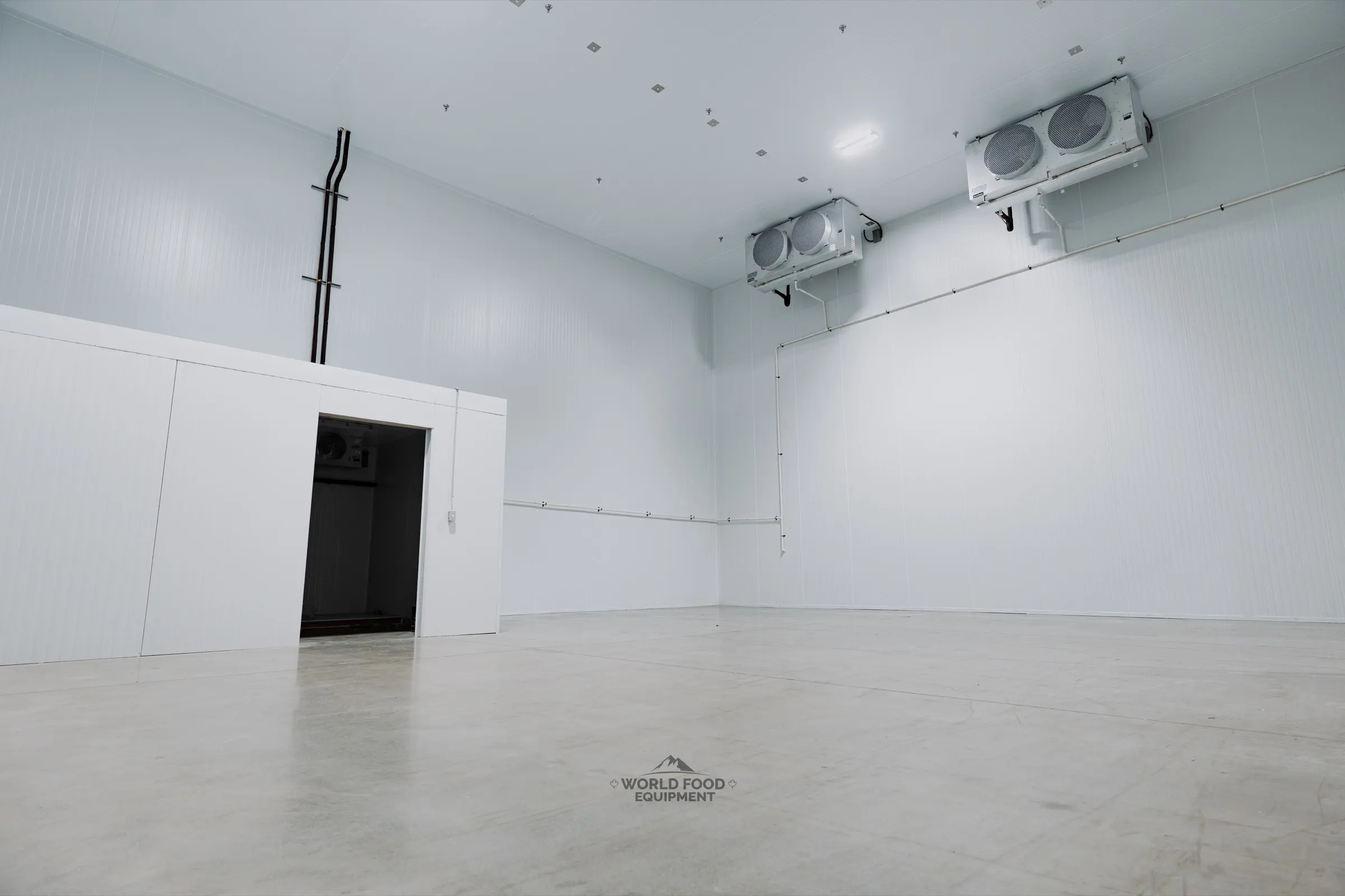 Cathedral-scale finished commercial walk-in cooler interior with insulated sliding door at the back wall, dual ceiling-mounted KeepRite evaporators visible on the right wall, white insulated panels and protective sheeting on the left, Pacer Air Freight install, Ontario, World Food Equipment