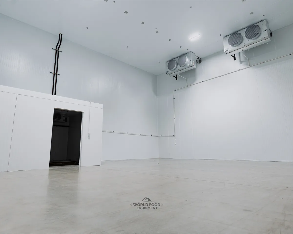 Large cathedral-scale finished commercial cold storage with tall white insulated panel walls and ceiling, a box-within-a-box inner cold room with an open doorway on the left, twin ceiling-mounted dual-fan evaporators on the right, polished concrete floor, Ontario commercial cold storage by World Food Equipment