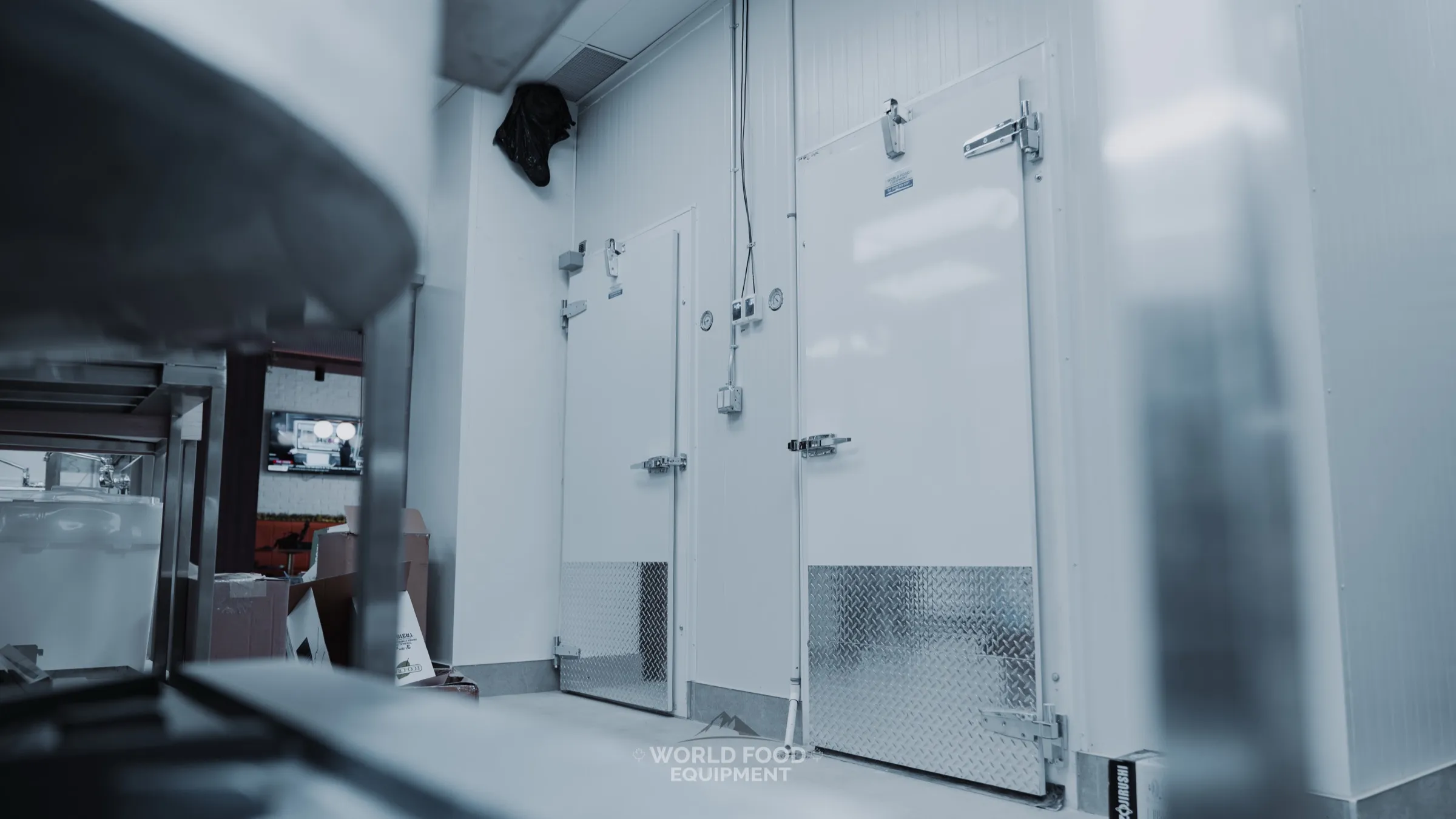 Recent World Food Equipment install at The Bagel House: twin-door insulated walk-in cooler in the back-of-house with stainless prep equipment visible in the foreground, Ontario restaurant kitchen, polished insulated panel envelope