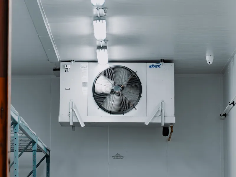 KRACK single-fan ceiling-mounted evaporator close-up inside the Food Junction Toronto walk-in cooler, white panel interior surrounding the unit, refrigeration line dropping down to the rooftop condenser.