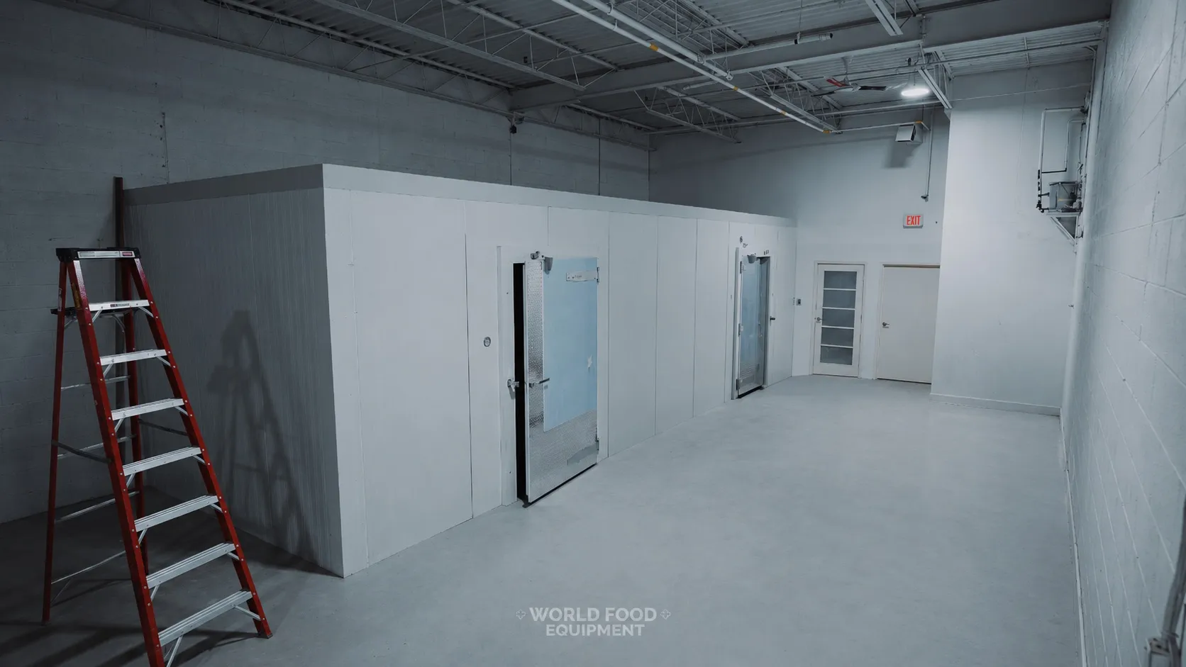 Finished commercial walk-in cooler envelope with two insulated swing doors at the front, one with a diamond-plate kickplate, an A-frame red step ladder staged on the left, raw concrete warehouse walls and ceiling with exposed overhead piping, polished concrete floor, Ontario commercial walk-in installation by World Food Equipment