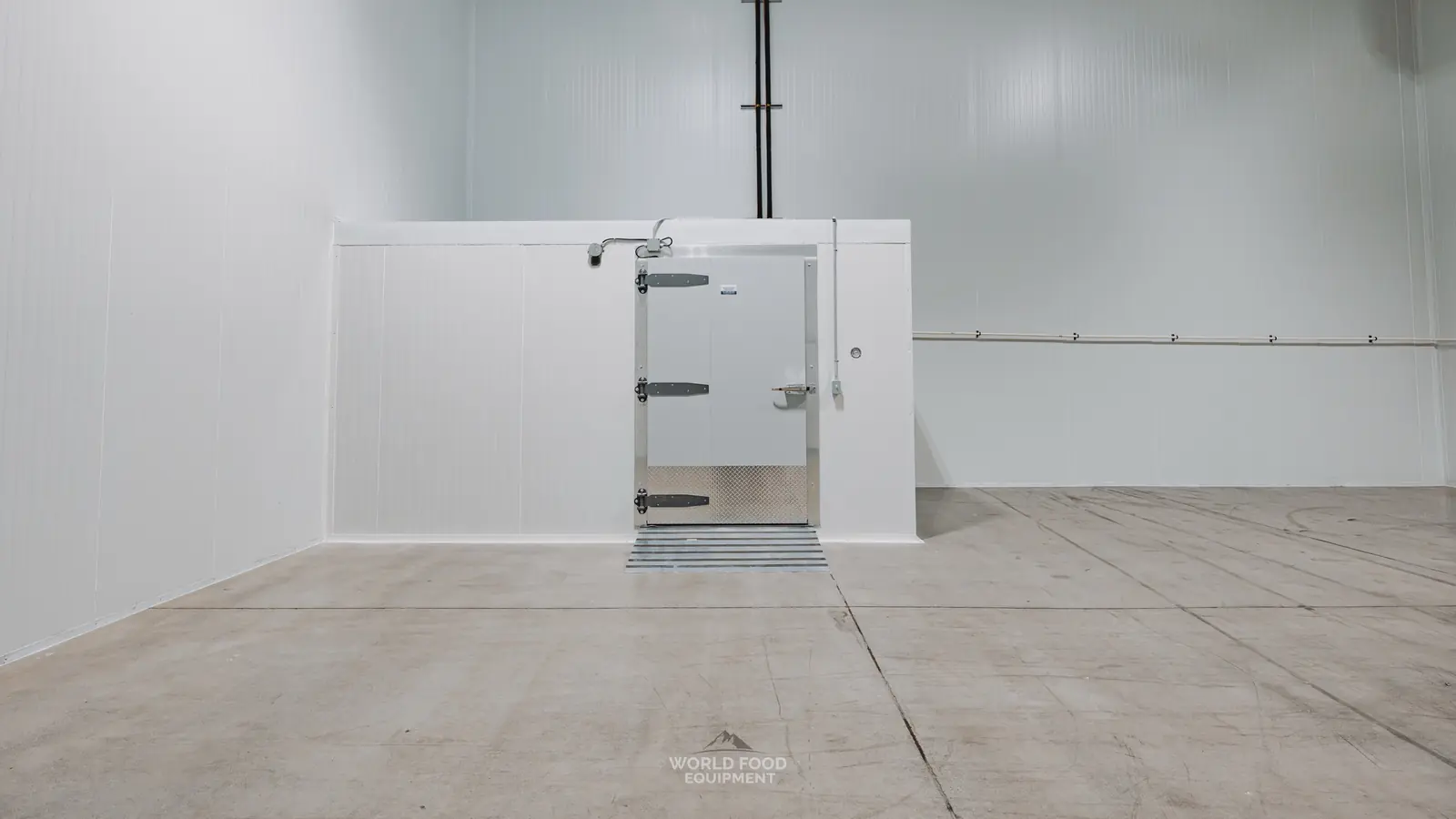 Finished white insulated walk-in box with a swing door, three cam-lift hinges, a diamond-plate kickplate and an aluminum threshold ramp, built by World Food Equipment inside a larger cold room at the Pacer Air Freight project in Ontario