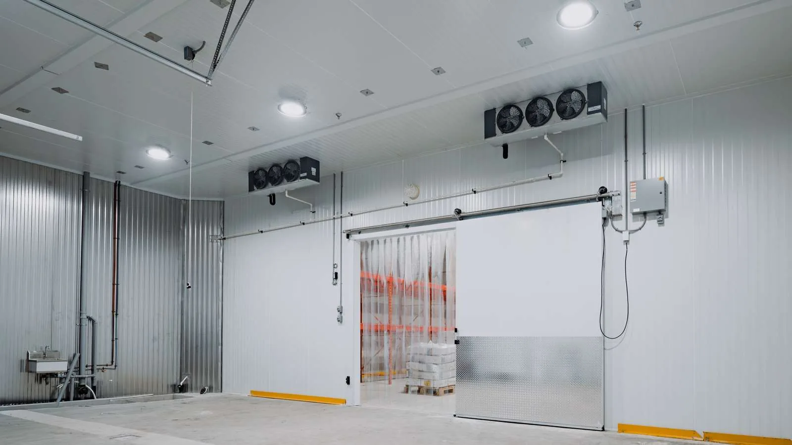 Finished walk-in cold room at a World Food Equipment install in Ontario, insulated sliding door with diamond-plate kick panel, strip curtain, and twin ceiling evaporators