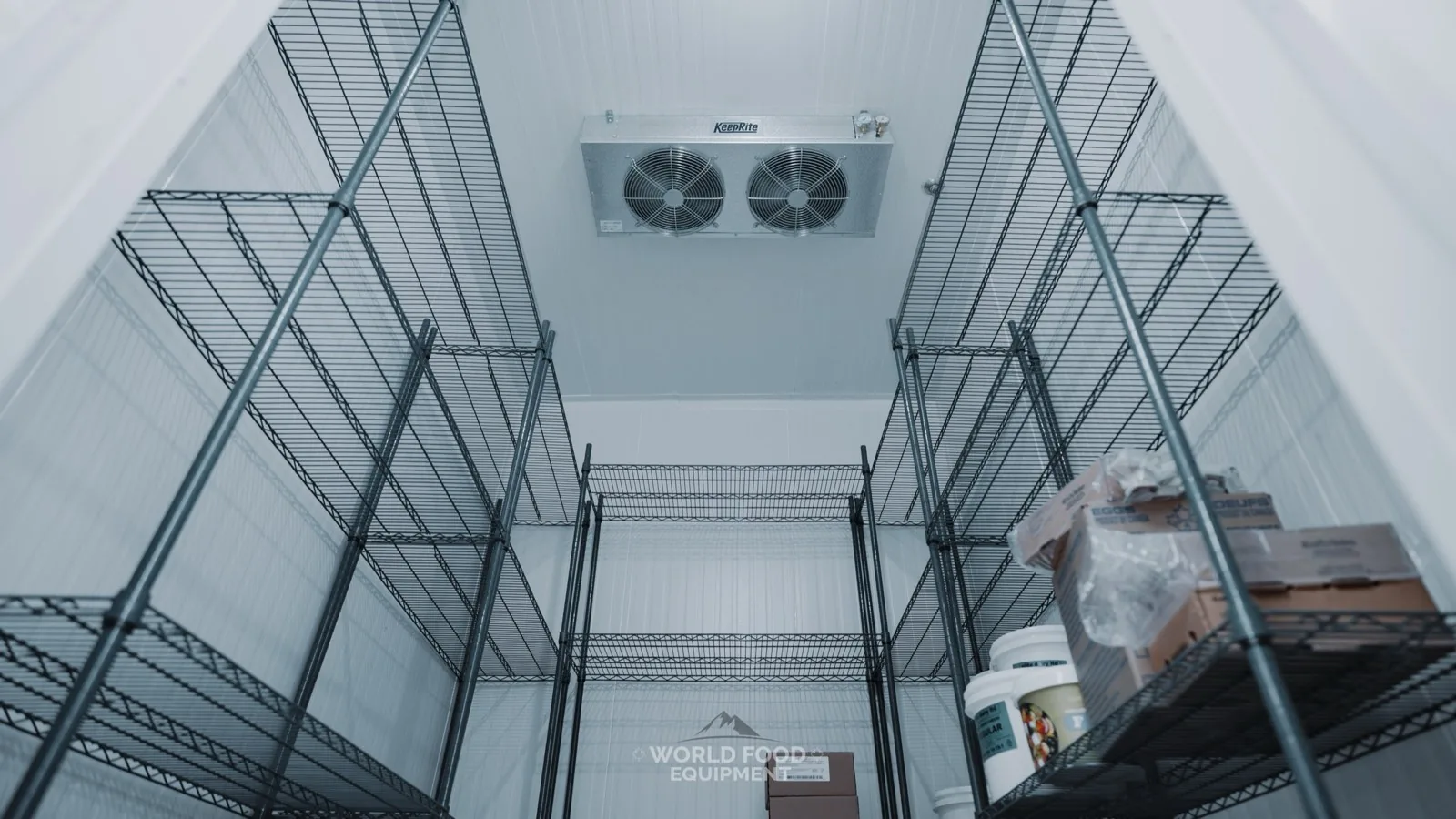 Interior of a WFE-installed walk-in cooler showing a KeepRite dual-fan ceiling evaporator above stocked wire shelving