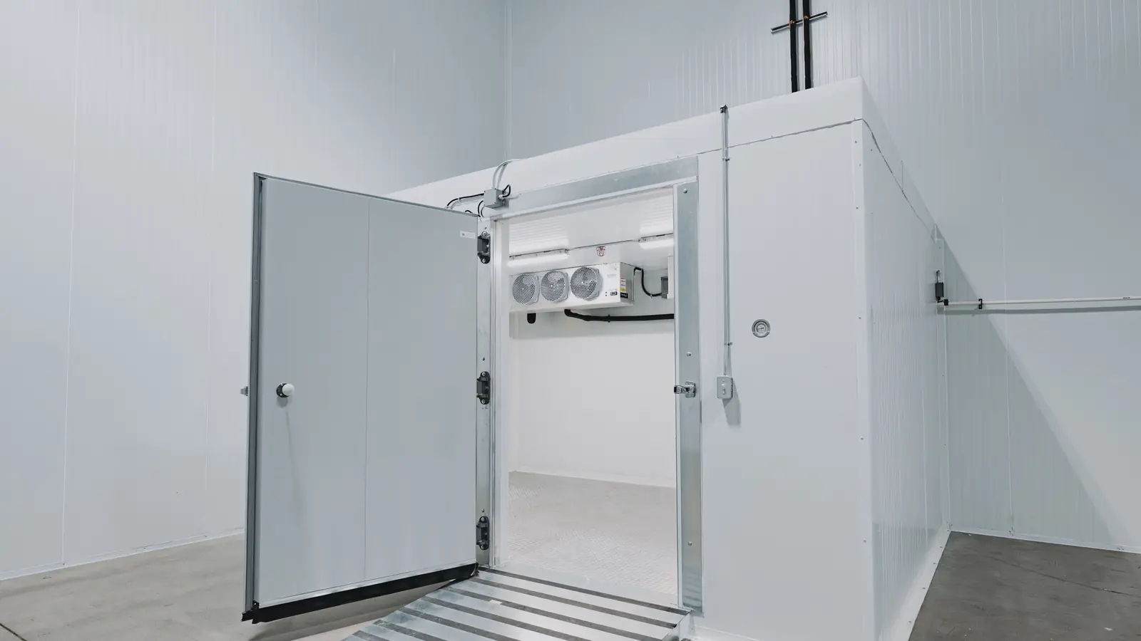 Walk-in cooler with the door swung open showing the hinges, latch, door sweep, threshold ramp, and evaporator inside, WFE install in Ontario