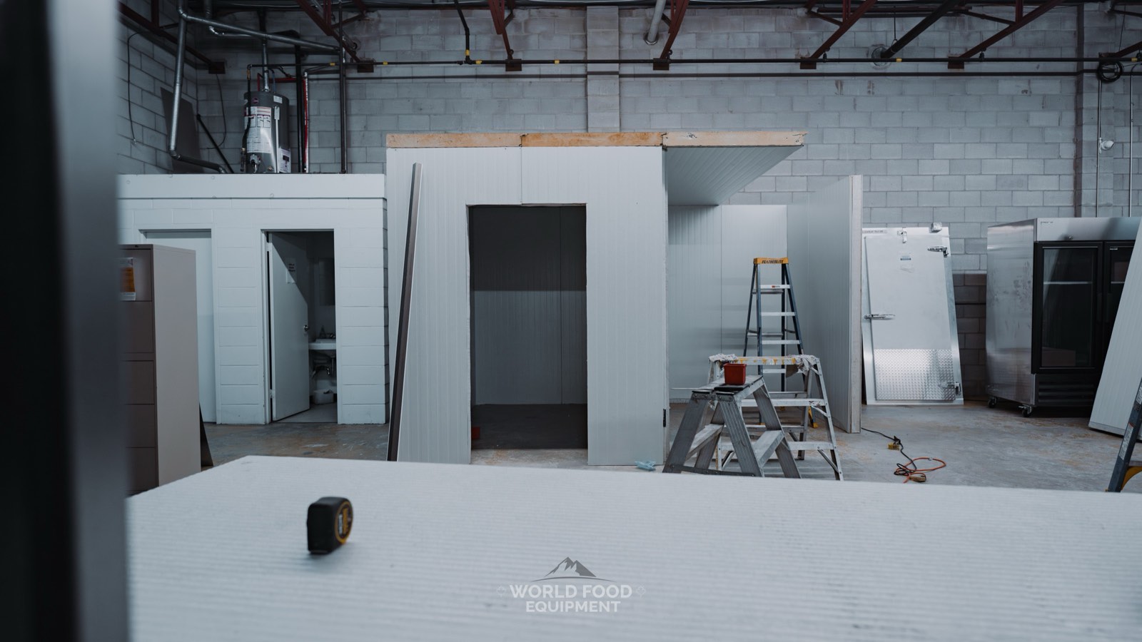 Two walk-in cold room boxes under construction side by side on a WFE build, insulated panels and walk-in doors staged around them