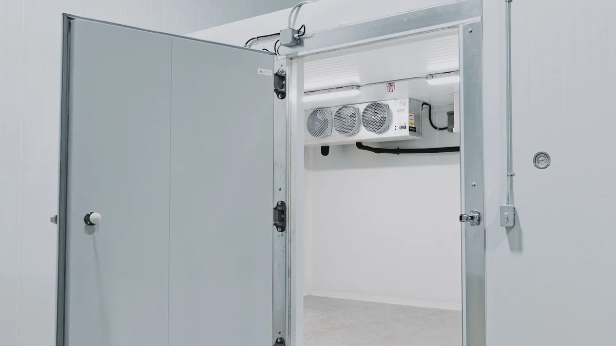 Open walk-in door showing the round inside safety release knob and cam-lift hinges, on a WFE cold room build in Mississauga