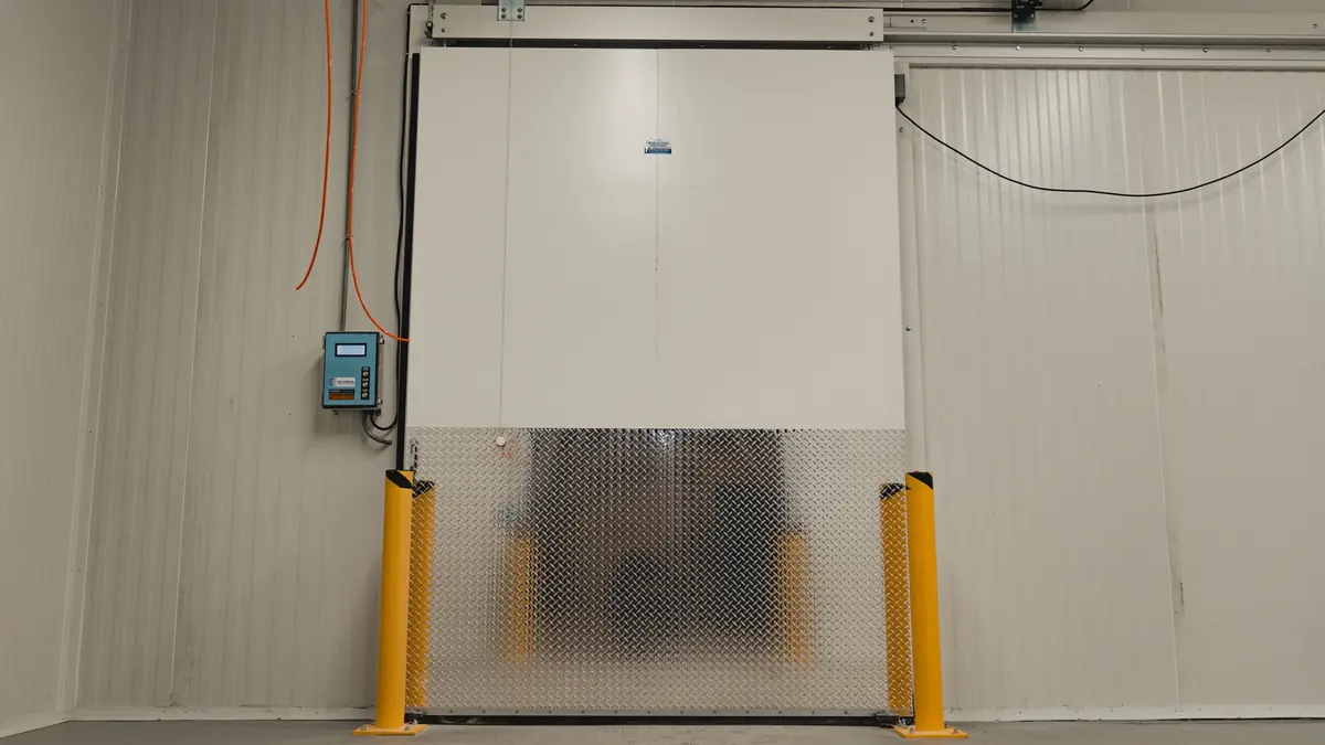 Automatic insulated sliding door with a diamond-plate kick panel, steel bollards, and a wall-mounted door control box on a 3,000 sq ft walk-in freezer build in Ontario
