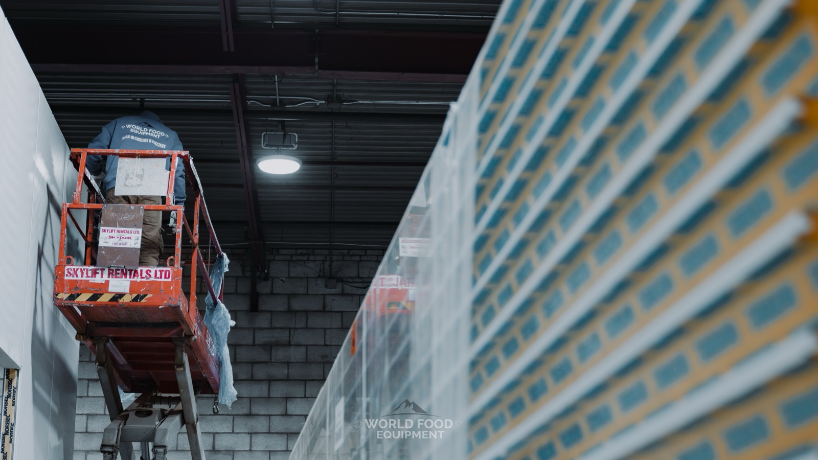 World Food Equipment installer on a scissor lift assembling Norbec insulated walk-in cooler panels at a cold storage build in Ontario
