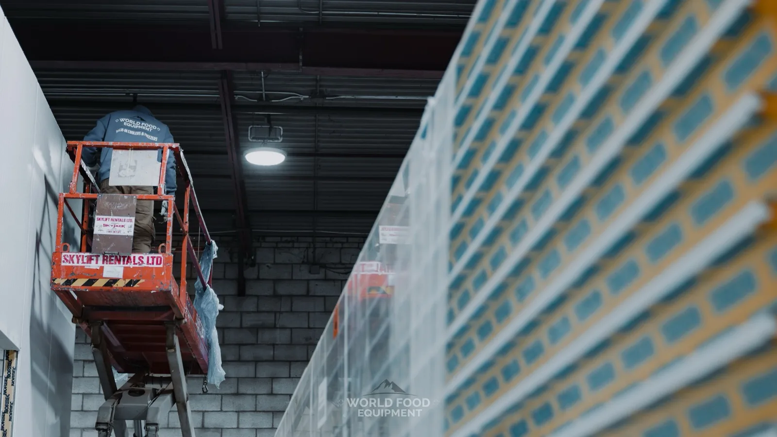 World Food Equipment installer on a scissor lift assembling Norbec insulated walk-in cooler panels at a cold storage build in Ontario